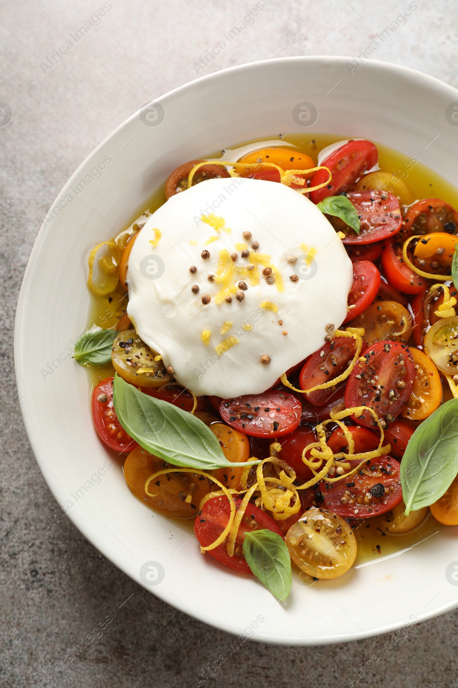 Photo of Delicious fresh burrata salad in bowl on gray textured table, top view