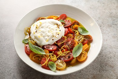 Photo of Delicious fresh burrata salad in bowl on gray textured table, closeup