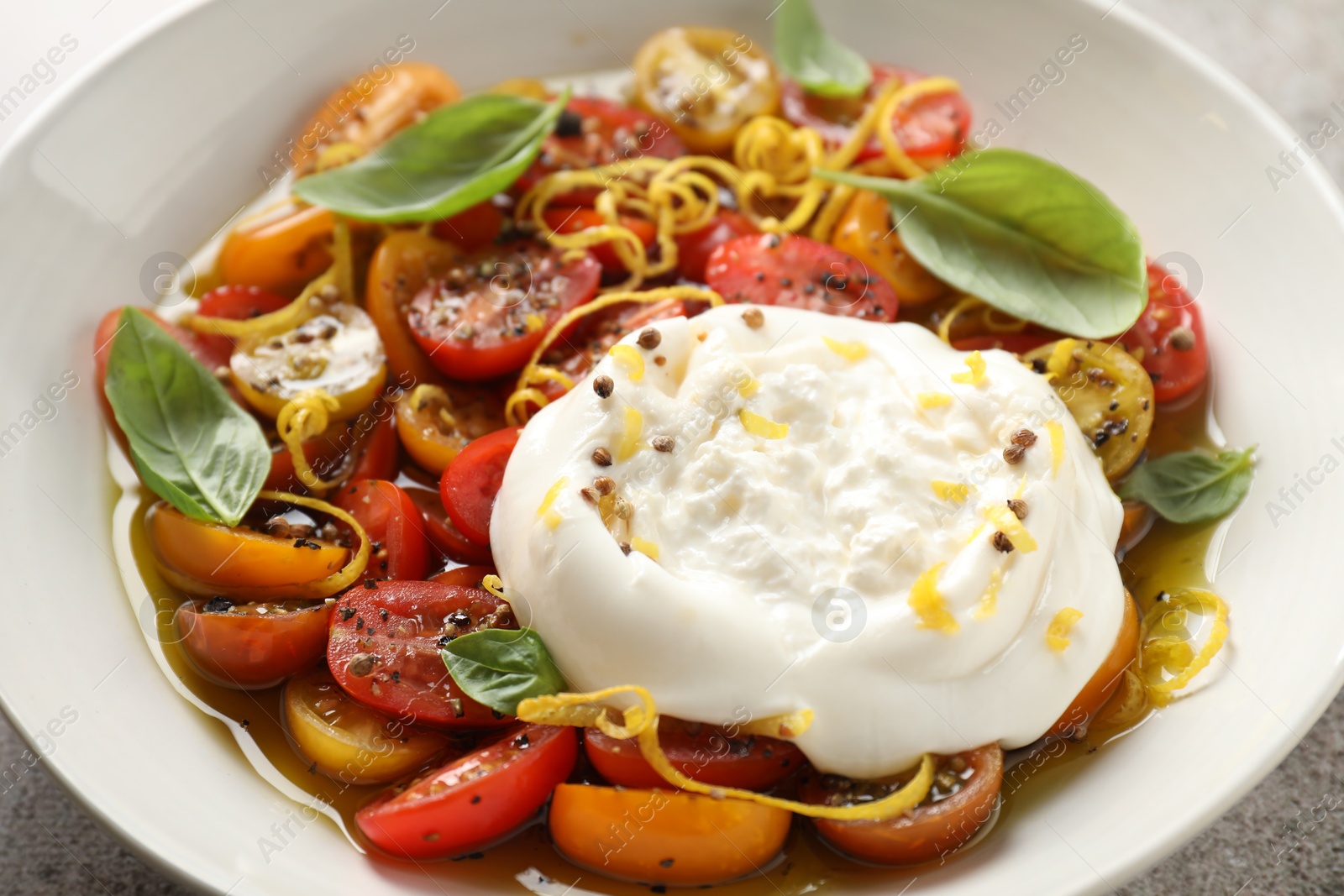 Photo of Delicious fresh burrata salad in bowl on table, closeup