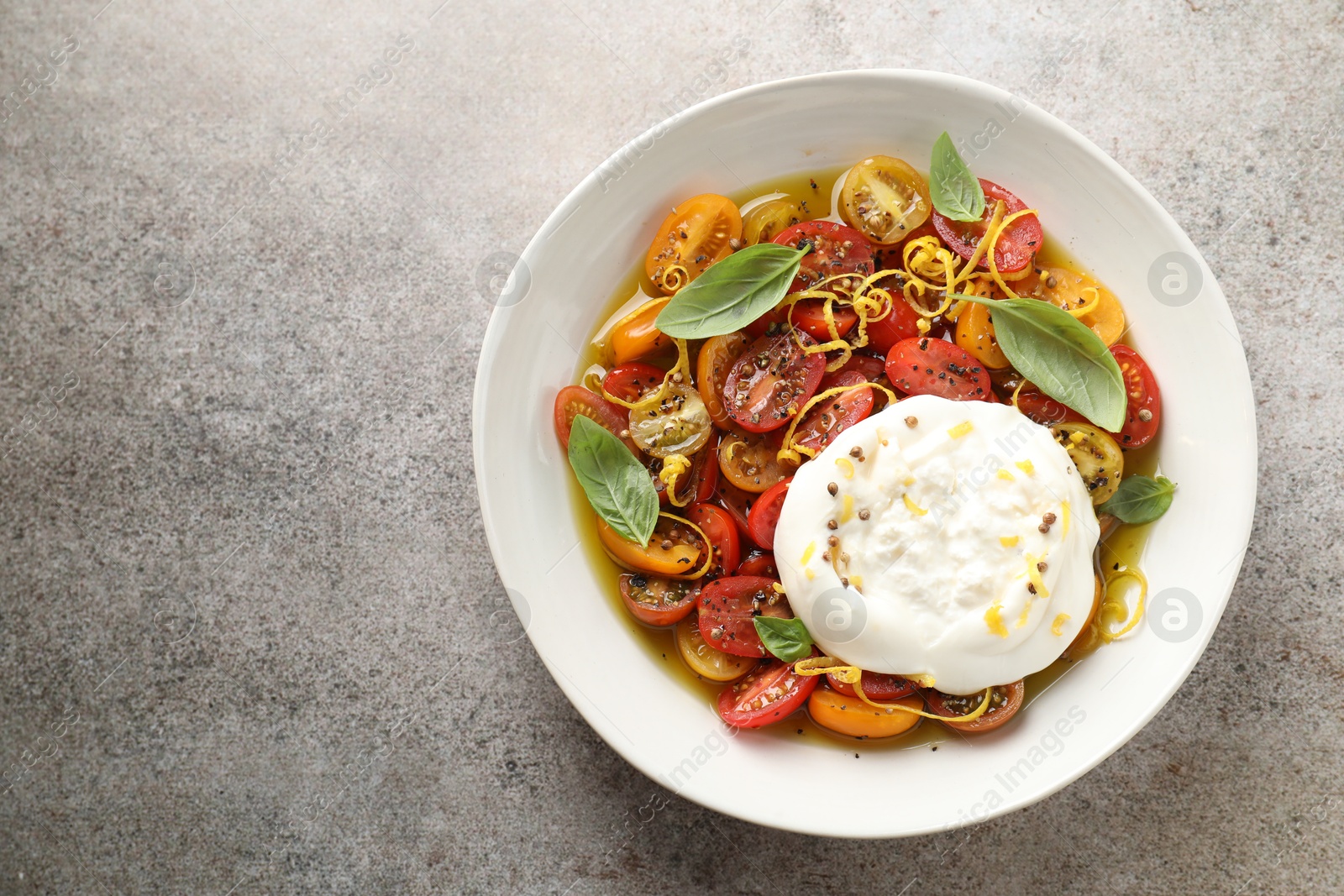 Photo of Delicious fresh burrata salad in bowl on gray textured table, top view. Space for text