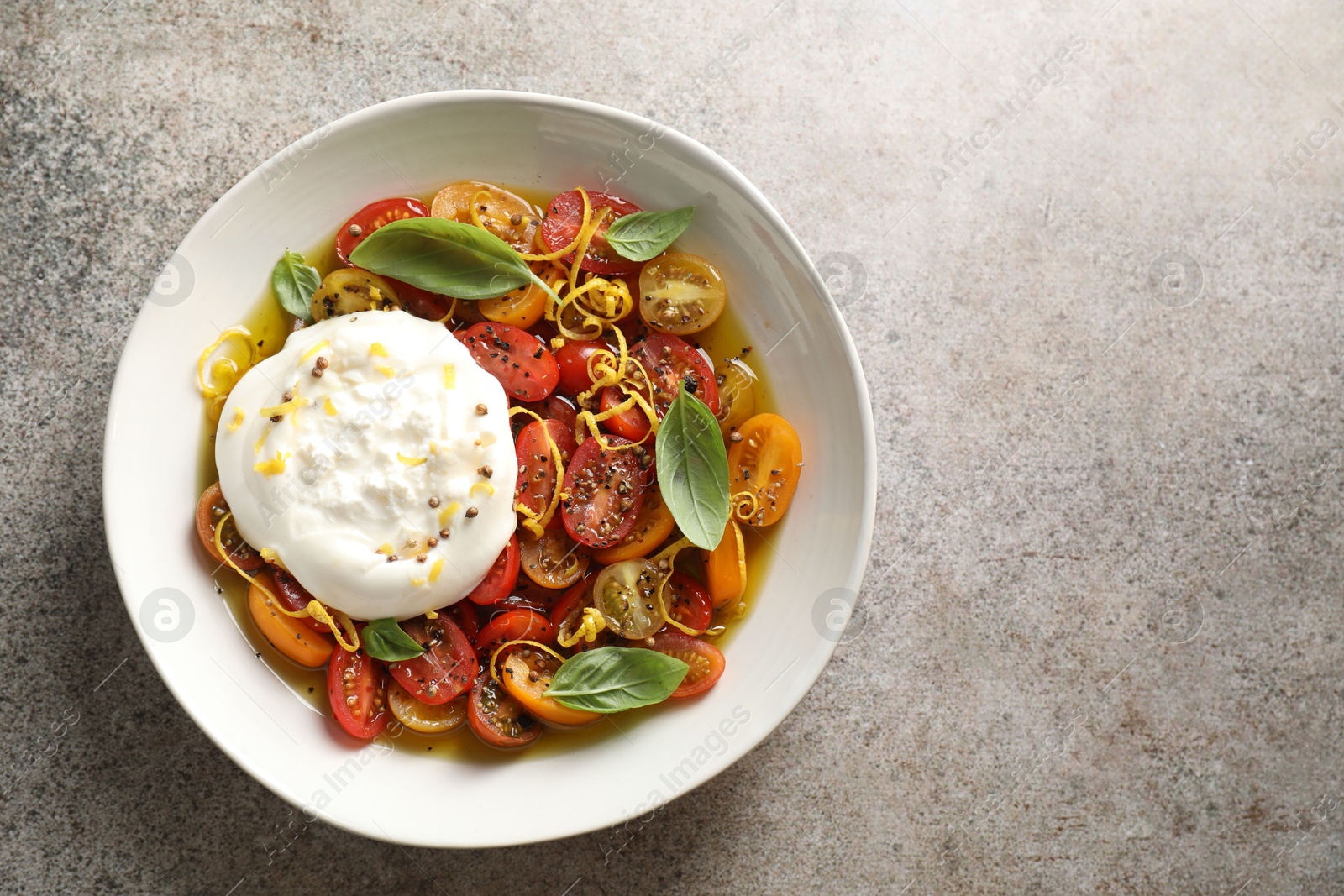 Photo of Delicious fresh burrata salad in bowl on gray textured table, top view. Space for text