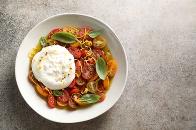 Photo of Delicious fresh burrata salad in bowl on gray textured table, top view. Space for text