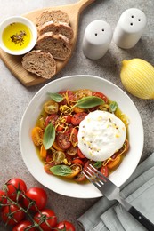 Photo of Delicious fresh burrata salad in bowl served on gray textured table, flat lay