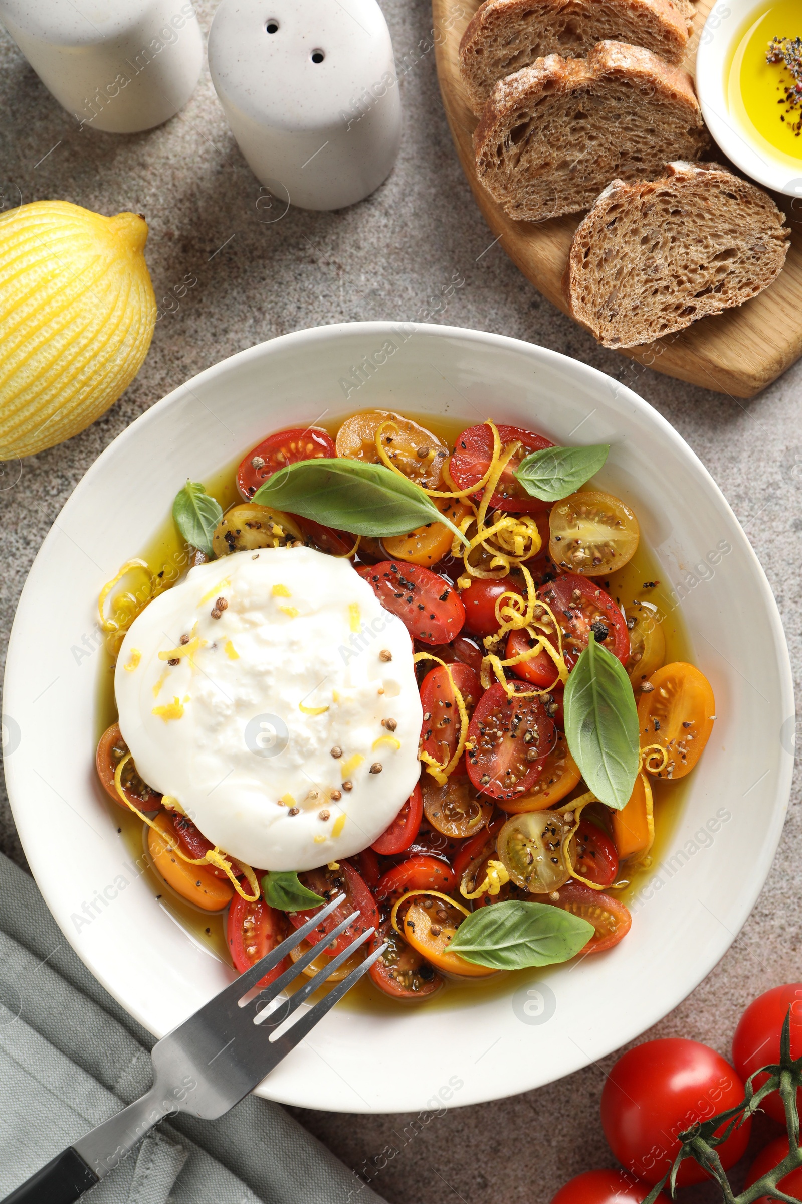 Photo of Delicious fresh burrata salad in bowl served on gray textured table, flat lay