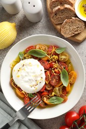 Photo of Delicious fresh burrata salad in bowl served on gray textured table, flat lay