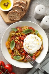 Photo of Delicious fresh burrata salad in bowl served on gray textured table, flat lay