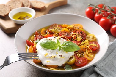 Photo of Delicious fresh burrata salad in bowl served on gray textured table, closeup