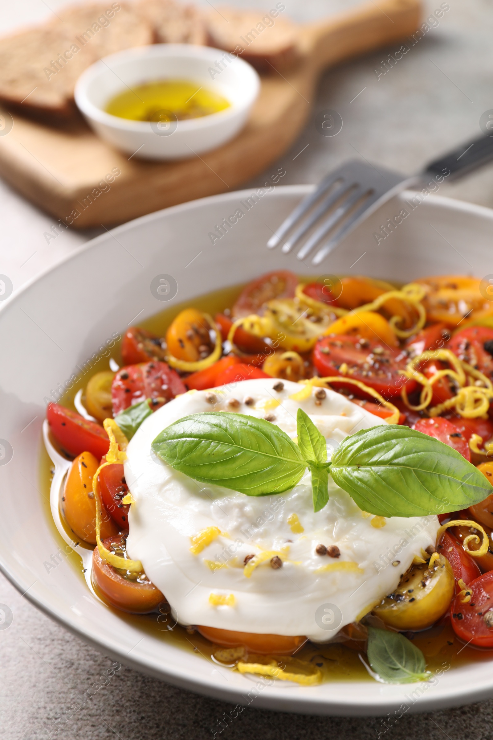 Photo of Delicious fresh burrata salad in bowl served on gray textured table, closeup