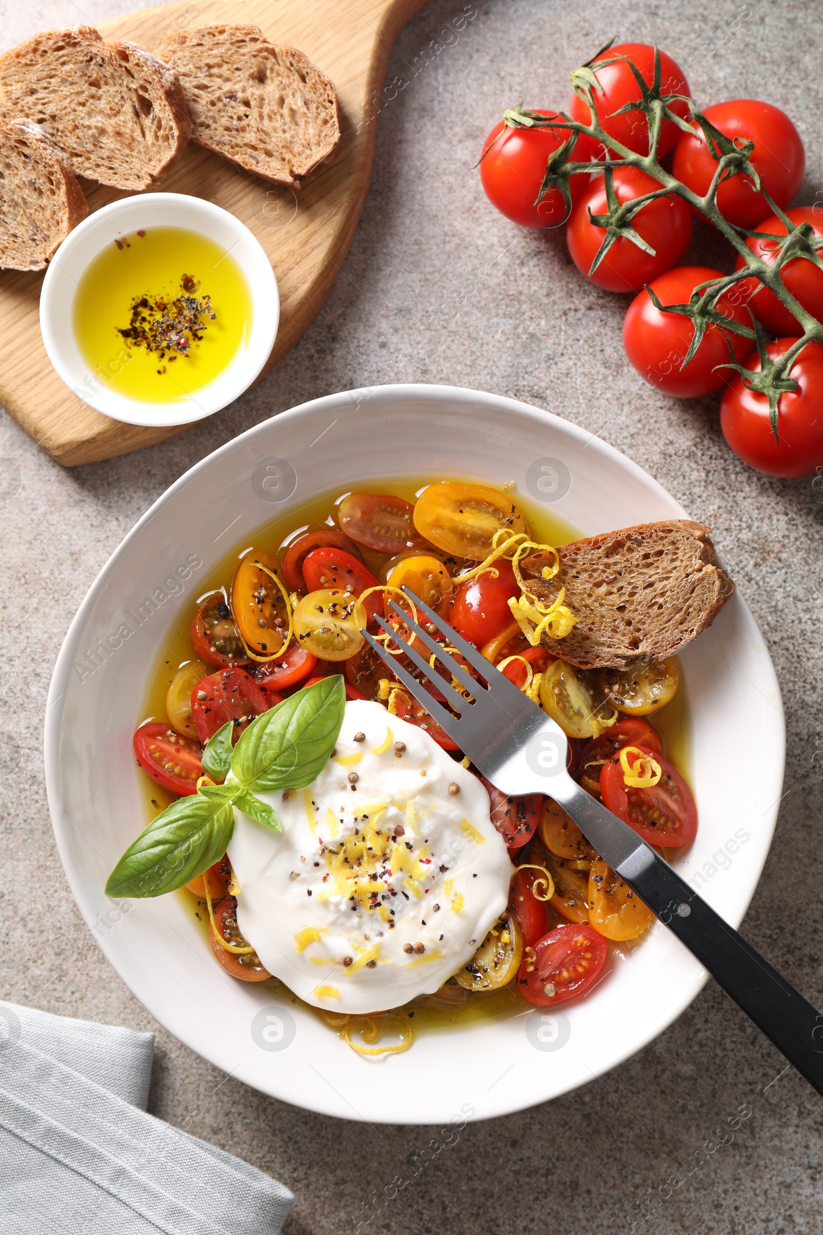 Photo of Delicious fresh burrata salad in bowl served on gray textured table, flat lay