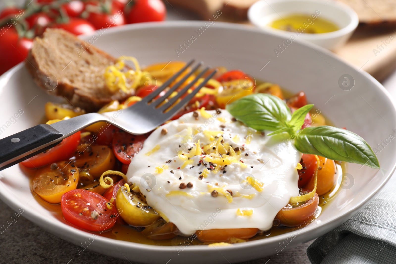 Photo of Delicious fresh burrata salad in bowl served on table, closeup