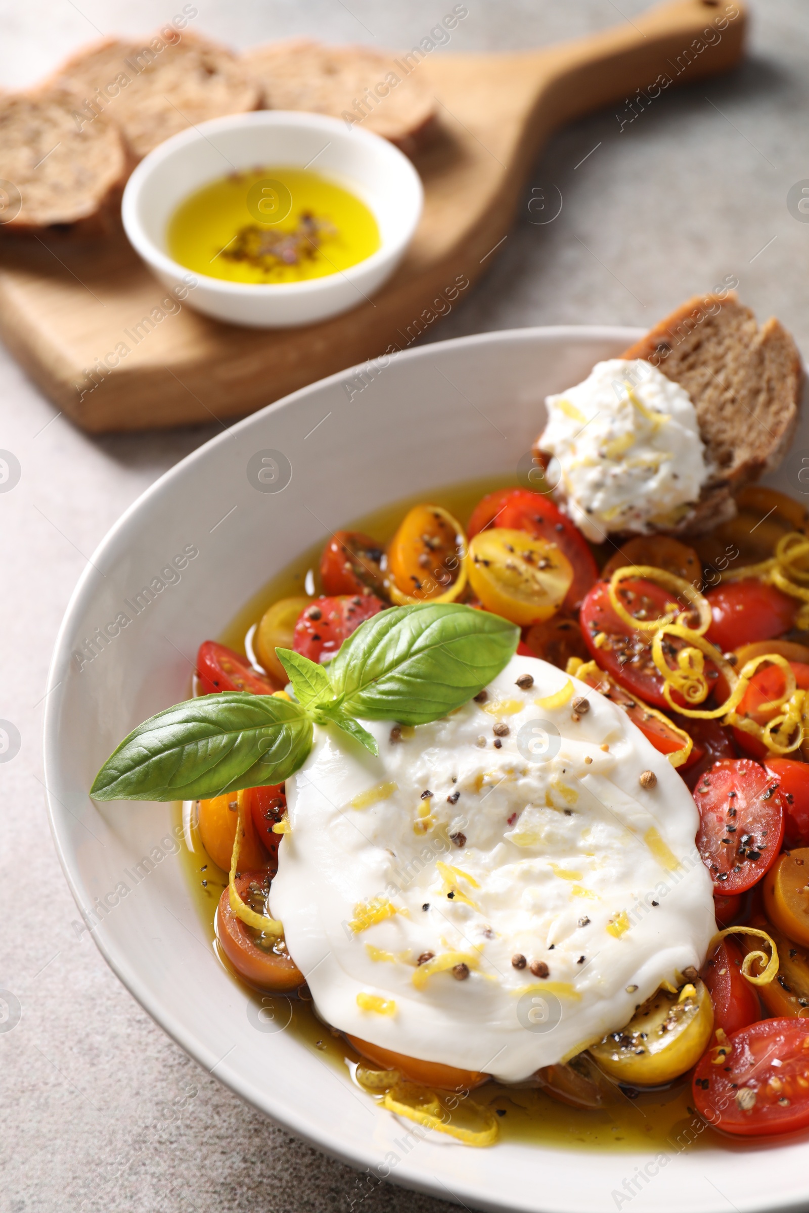 Photo of Delicious fresh burrata salad in bowl on gray table, closeup