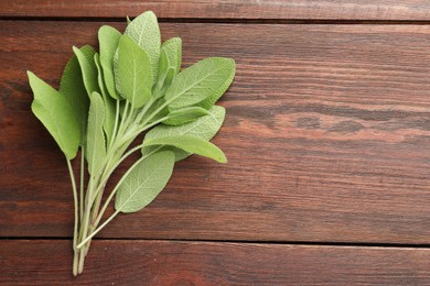 Photo of Green sage leaves on wooden table, top view. Space for text