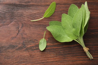 Photo of Bunch of green sage leaves on wooden table, top view. Space for text