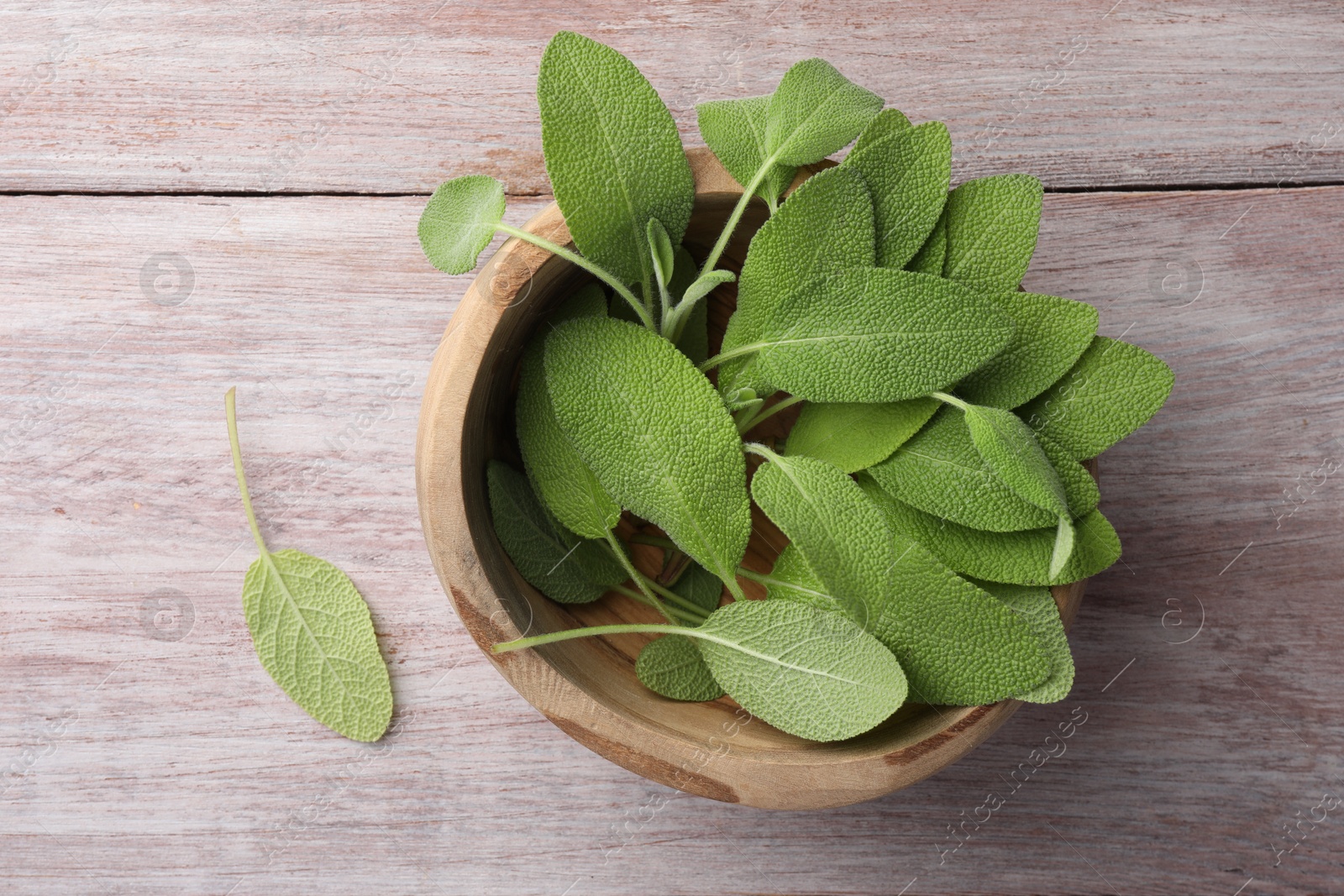 Photo of Green sage leaves in bowl on color wooden table, top view