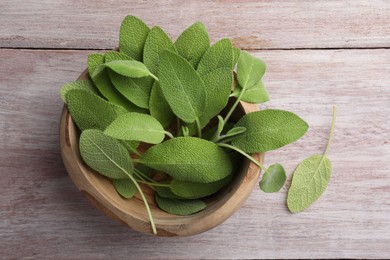 Photo of Green sage leaves in bowl on color wooden table, top view