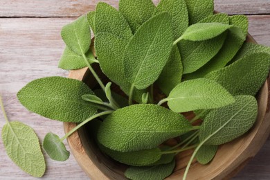 Photo of Green sage leaves in bowl on color wooden table, top view