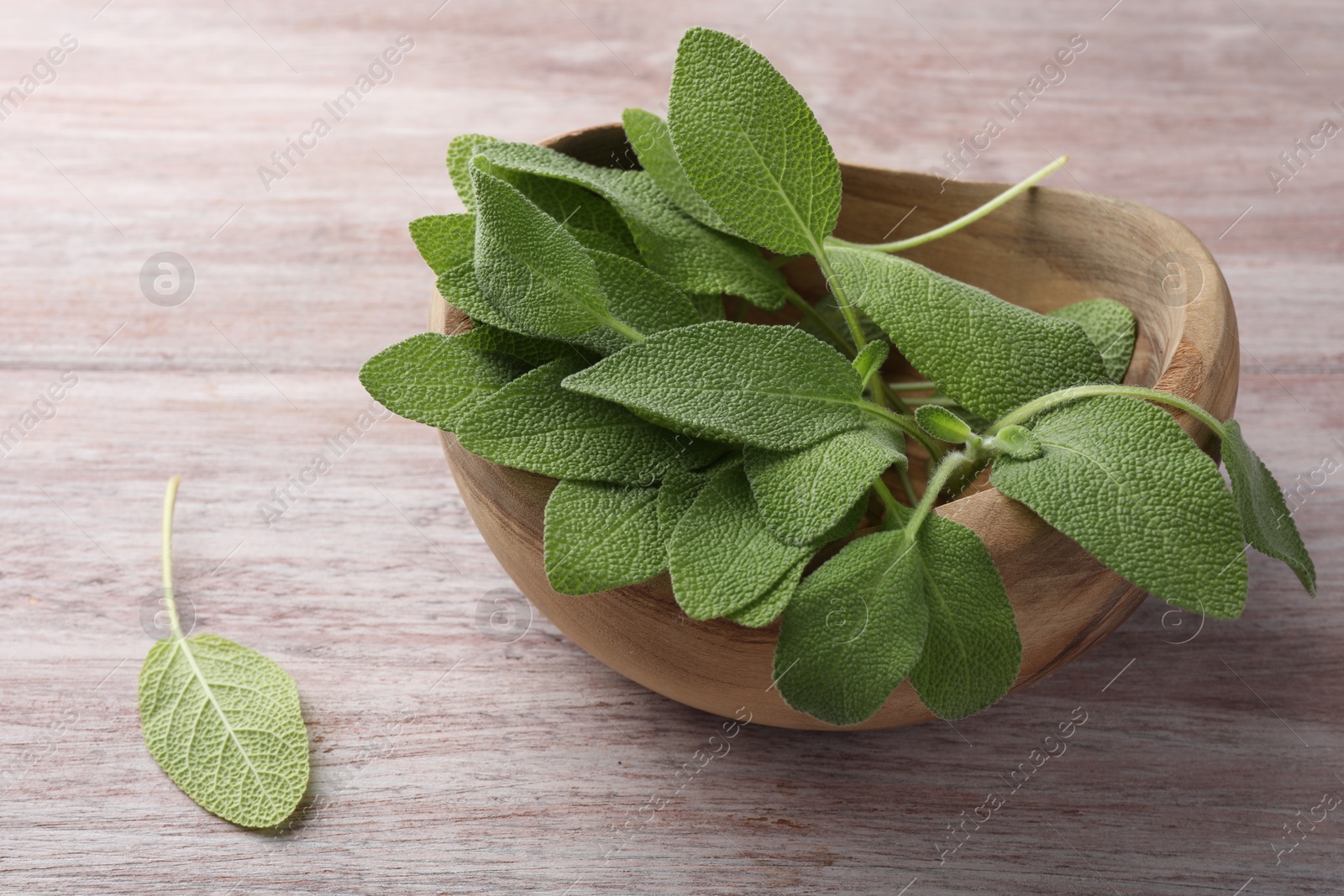 Photo of Green sage leaves in bowl on color wooden table, closeup