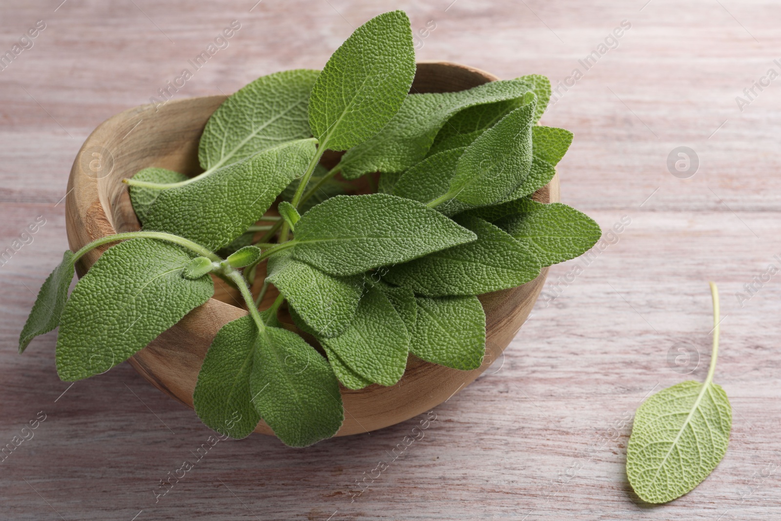 Photo of Green sage leaves in bowl on color wooden table, closeup