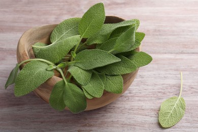 Photo of Green sage leaves in bowl on color wooden table, closeup