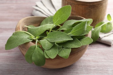 Photo of Green sage leaves in bowl on color wooden table, closeup