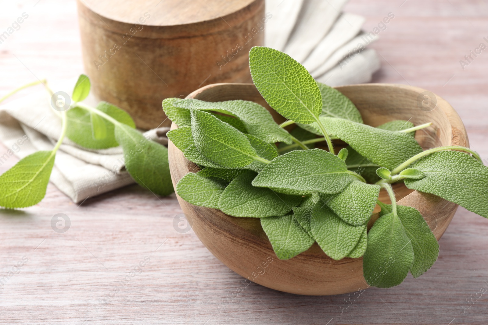 Photo of Green sage leaves in bowl on color wooden table, closeup