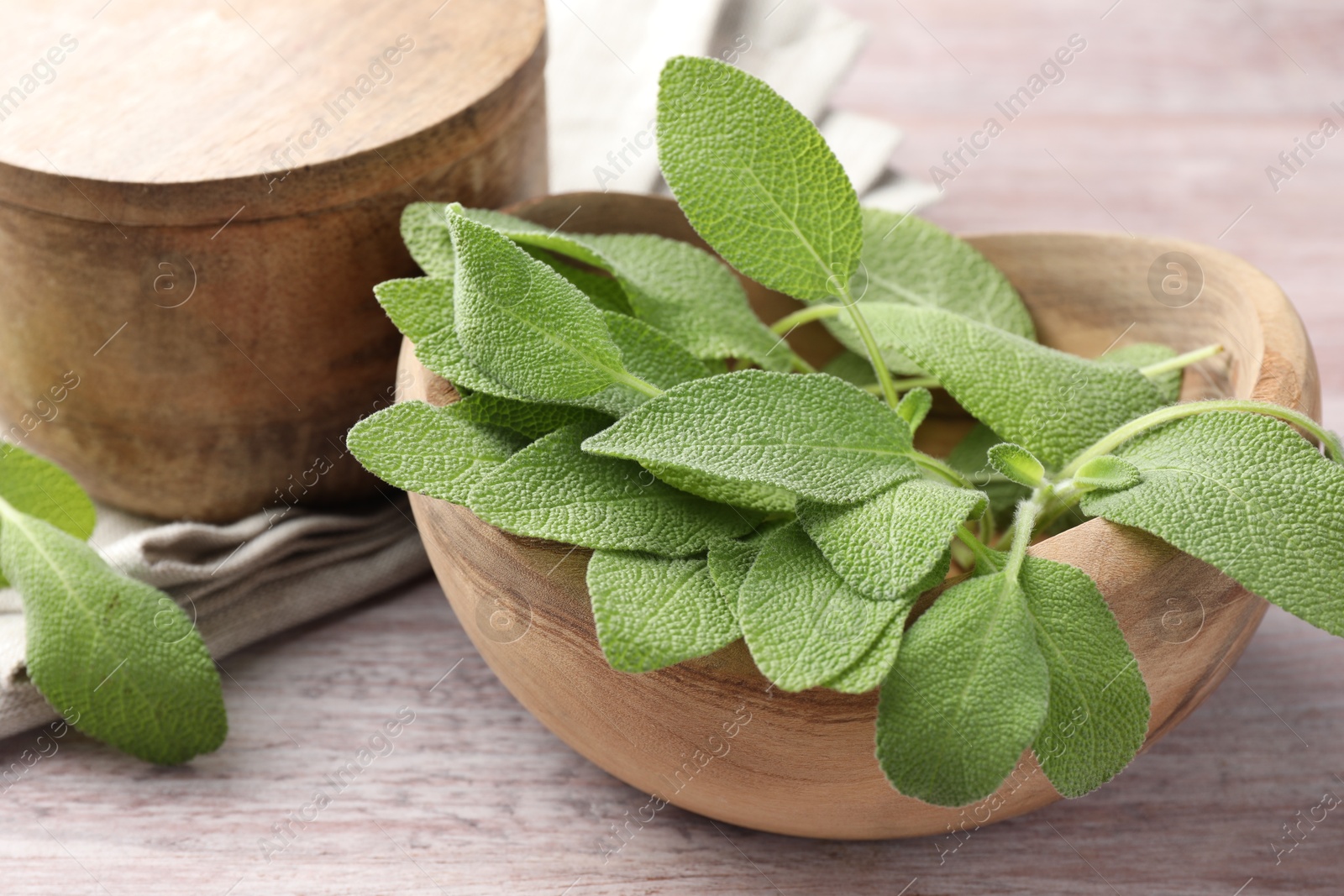 Photo of Green sage leaves in bowl on color wooden table, closeup