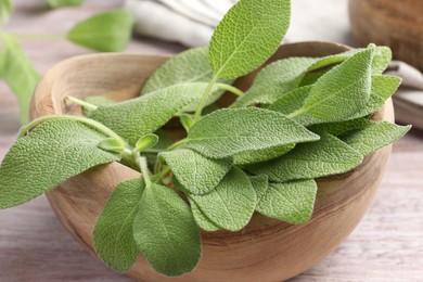 Photo of Green sage leaves in bowl on color table, closeup