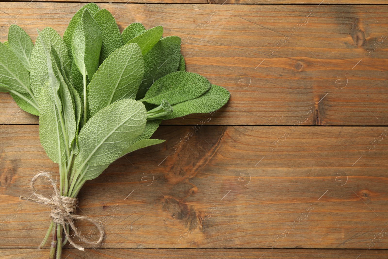 Photo of Bunch of green sage leaves on wooden table, top view. Space for text