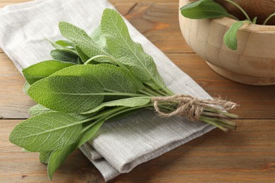 Photo of Bunch of green sage leaves on wooden table, closeup