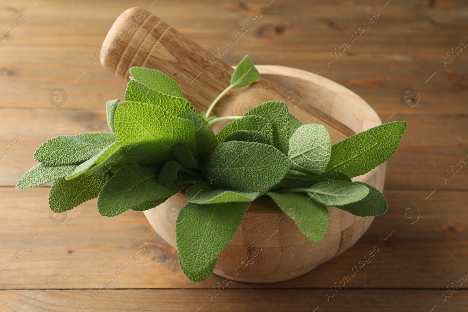 Photo of Green sage leaves and pestle in mortar on wooden table, closeup