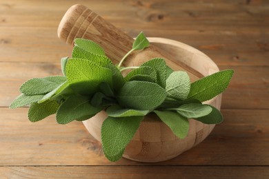 Photo of Green sage leaves and pestle in mortar on wooden table, closeup