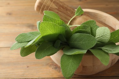 Photo of Green sage leaves and pestle in mortar on wooden table, closeup