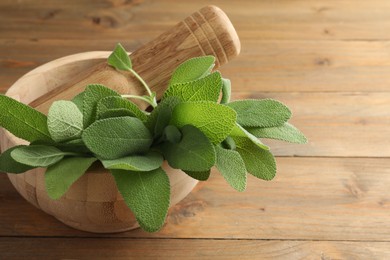 Photo of Green sage leaves and pestle in mortar on wooden table, closeup