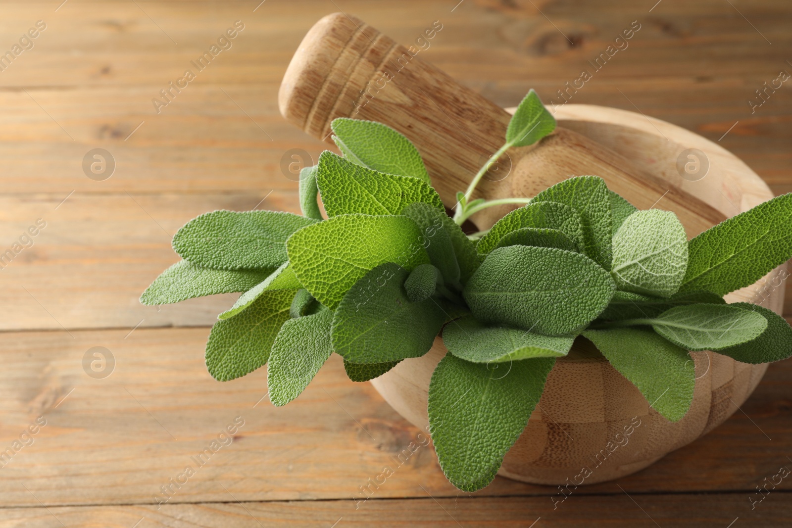 Photo of Green sage leaves and pestle in mortar on wooden table, closeup