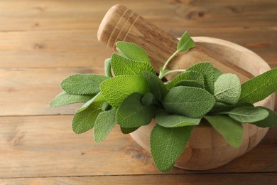 Photo of Green sage leaves and pestle in mortar on wooden table, closeup