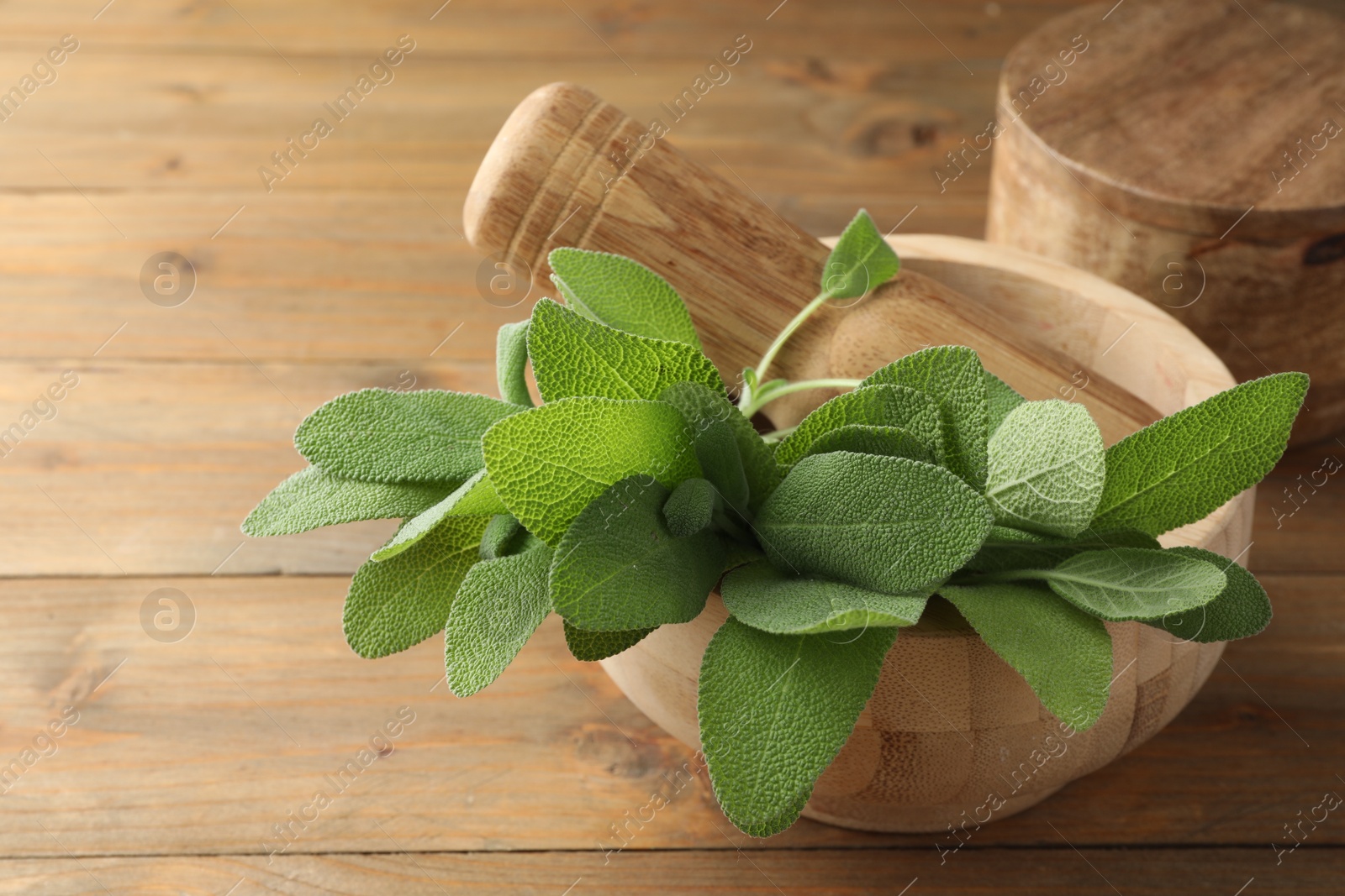 Photo of Green sage leaves and pestle in mortar on wooden table, closeup