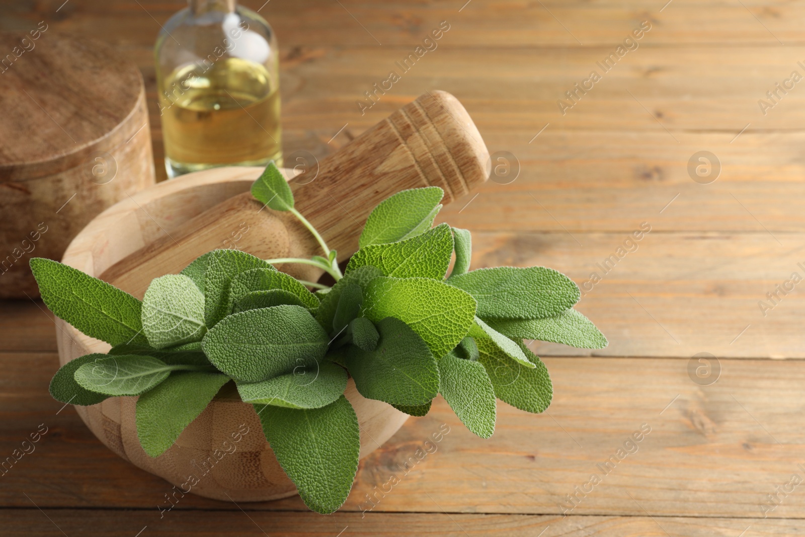 Photo of Green sage leaves and pestle in mortar on wooden table, closeup. Space for text