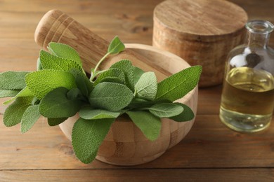 Photo of Green sage leaves and pestle in mortar on wooden table, closeup