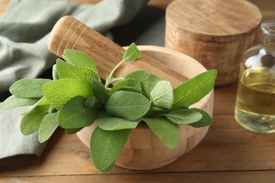 Photo of Green sage leaves and pestle in mortar on wooden table, closeup