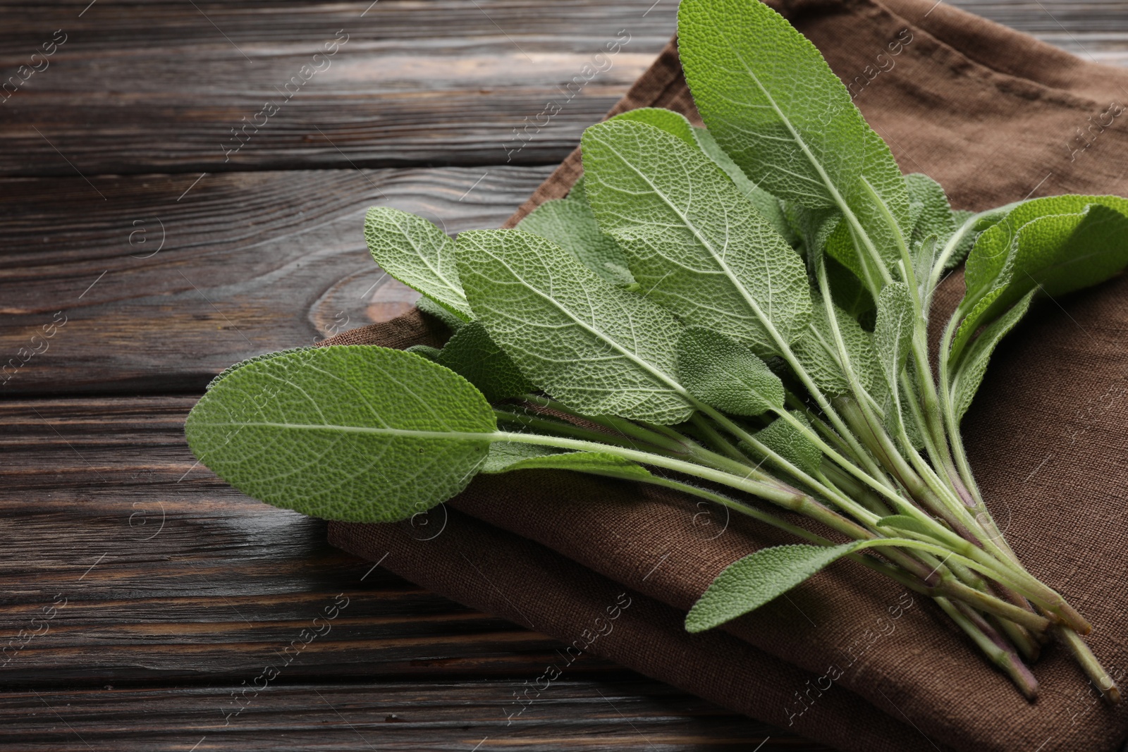 Photo of Napkin with green sage leaves on wooden table, closeup