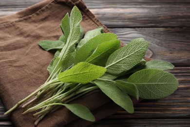 Photo of Napkin with green sage leaves on wooden table, closeup