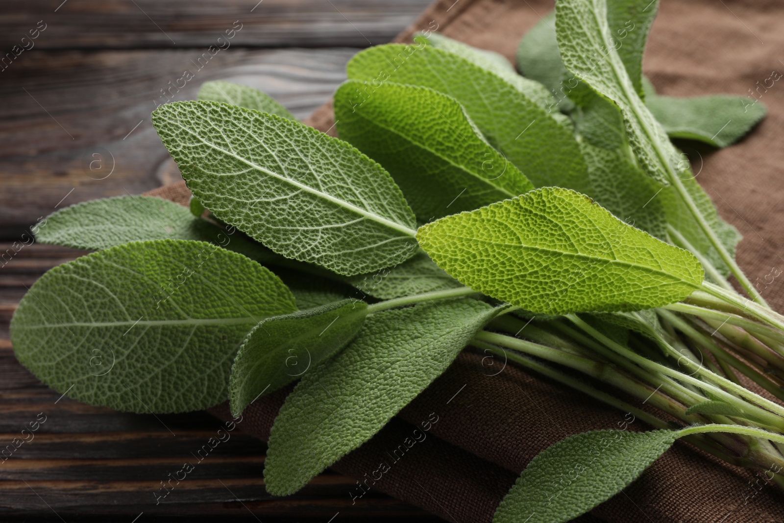 Photo of Napkin with green sage leaves on wooden table, closeup