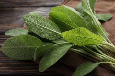 Photo of Napkin with green sage leaves on wooden table, closeup