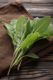 Photo of Napkin with green sage leaves on wooden table, closeup