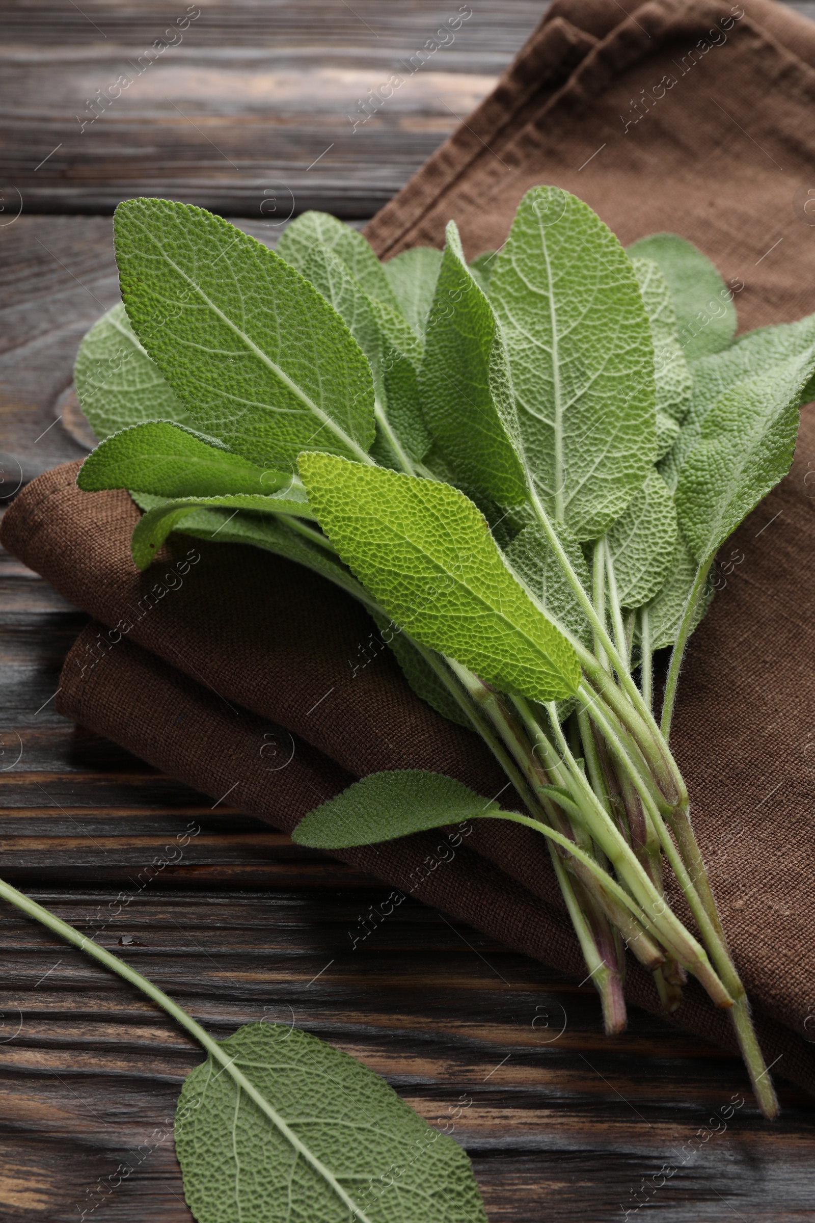 Photo of Napkin with green sage leaves on wooden table, closeup