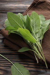 Photo of Napkin with green sage leaves on wooden table, closeup