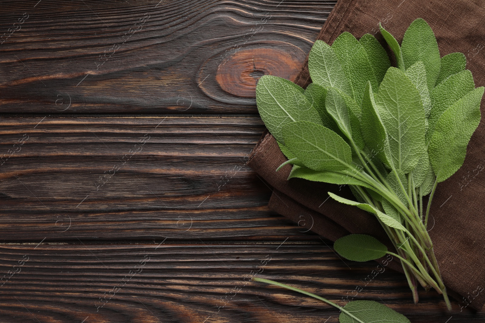 Photo of Napkin with green sage leaves on wooden table, top view. Space for text