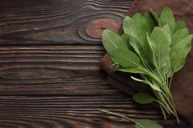 Photo of Napkin with green sage leaves on wooden table, top view. Space for text