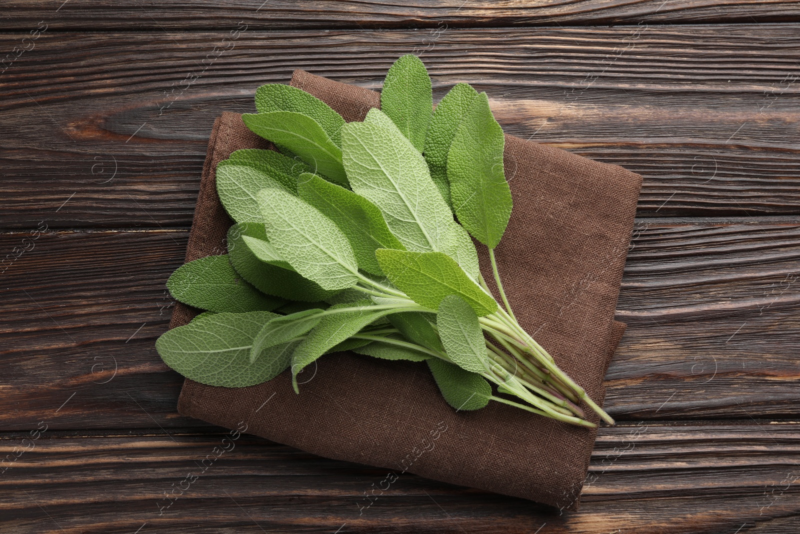 Photo of Napkin with green sage leaves on wooden table, top view