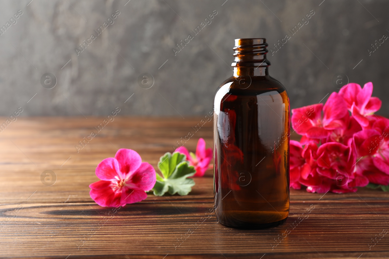 Photo of Geranium essential oil in bottle and beautiful flowers on wooden table